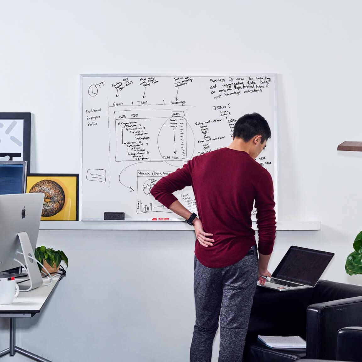 portrait of person at laptop in front of whiteboard on office wall